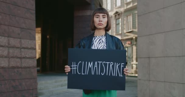 Portret van een jonge hippe vrouw met een kartonnen plakkaat met een hashtag voor klimaatstakingen op straat. Aantrekkelijk meisje dat beweging voor ecologie en schone planeet ondersteunt. Concept van het redden van de Aarde. — Stockvideo