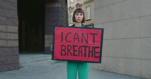 Jong meisje met een neusring met een plakkaat met ademhaling. Millennial serieuze vrouw ondersteunen beweging tegen politiegeweld en racisme terwijl ze op straat staan.Zoom in. — Stockvideo