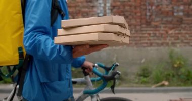 Banliyö caddesinde yürürken pizza paketlerini taşıyan bisikletli kurye görüntüsü. Servis elemanı müşteriye sipariş verirken bisikleti itiyor..