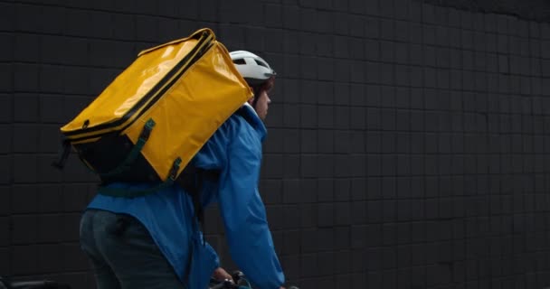 Zadní pohled na mužského kurýra s přepravou potravin batoh jízdu na kole na ulici. Muž v ochranné cyklistické helmě doručuje objednávku zákazníkovi. Koncepce dodávky potravin. — Stock video