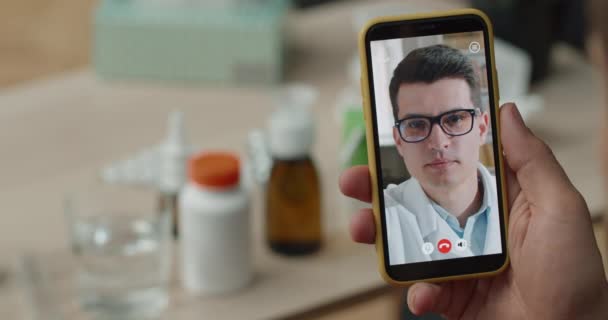 Sopra vista spalla della persona mani tenendo smartphone e parlando con il medico femminile maturo. Vista da vicino del paziente malato che ha una consultazione medica online. Concetto di telemedicina. — Video Stock