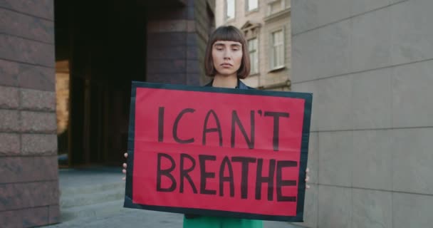 Portré női aktivistáról, aki kartondobozt tart, és alig kapok levegőt. Millenniumi lány támogatja mozgalom ellen rendőrségi brutalitás és rasszizmus, miközben áll a város utcáján. — Stock videók