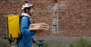 Ulaşım çantalı erkek kuryenin banliyö caddesinde yürürken bisiklet sürüşünün yan görüntüsü. Sipariş verirken pizza kutuları taşıyan koruyucu bisiklet kasklı bir adam..