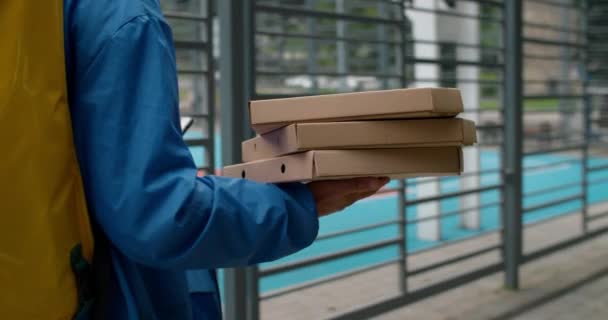 Kurier przewożący pudełka po pizzy podczas dostarczania zamówienia do klienta. Powrót do widoku z przodu osoby dostawy z workiem transportowym żywności za pomocą smartfona podczas spaceru na świeżym powietrzu. — Wideo stockowe