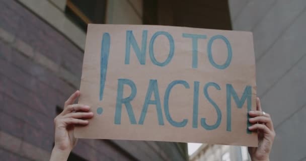 Στενή θέα των γυναικείων χεριών που σηκώνουν χαρτονένια πινακίδα με όχι στο ρατσισμό στην οδό Σίτυ. Ακτιβιστής υπέρ της ισότητας των ανθρωπίνων δικαιωμάτων. Έννοια των ανθρώπων και προβλήματα socail. — Αρχείο Βίντεο