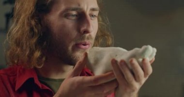 Sanat objesi yaratmak için çalışan genç ve tutkulu erkek heykeltraşa yakından bakın. Milenyum adamı elinde beyaz kilden bir ayak tutuyor ve tozunu üflüyor. Sanat eseri kavramı.