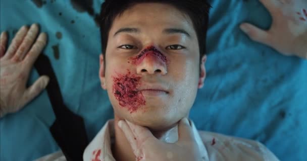 Junger Mann mit Blut- und Kopfverletzungen lächelnd auf Krankenhaustrage liegend. Sanitäter überprüfen den Puls eines Mannes mit Traumata auf dem Weg in den Operationssaal. Gesundheitskonzept. — Stockvideo