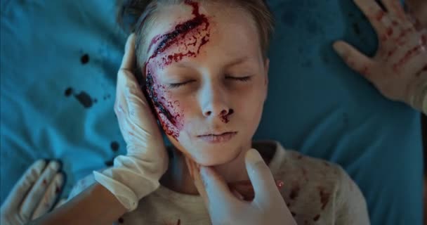 Närbild av paramedicinsk kontroll av hjärtslag till liitle pojke med sår och blod på huvudet.Ovanifrån av barn med skador som dör när du ligger på sjukhus bår på väg till operationssalen. — Stockvideo