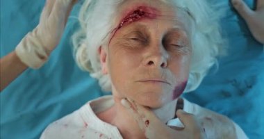 Kan ve kafa travması olan yaşlı bir kadının hastaneye giderken sedyede yattığını gördüm. Sağlık görevlileri ambulansta yaralanan olgun bir kadına kalp atış hızını ölçüyorlar..