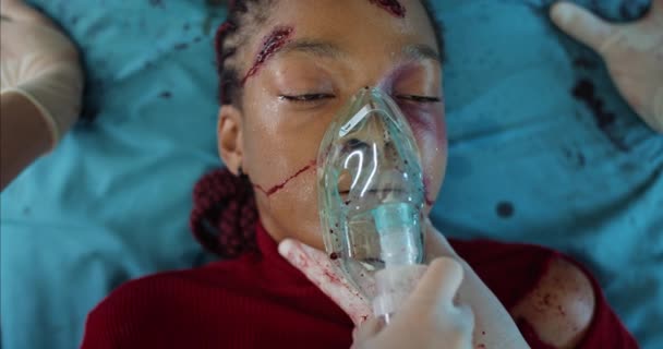 I paramedici controllano la frequenza cardiaca e tolgono la maschera per l'inalazione di ossigeno dal viso della giovane donna. Afro ragazza americana con traumi alla testa che muore mentre giace sulla barella dell'ospedale in ambulanza. — Video Stock