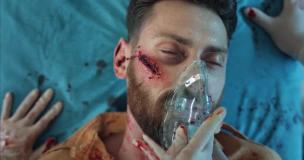 Närbild av ambulanspersonal händer sätta på syre inhalation mask på skäggig man ansikte. medvetslös kille i 40-årsåldern med skalltrauman liggande på sjukhusbår i ambulans. — Stockvideo