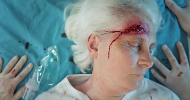 Close up of elderly woman with head injuries lying on medical stratcher in ambulance. Mature unconscious lady with wound and blood on her head riding to hospital after accident. — Stock Video