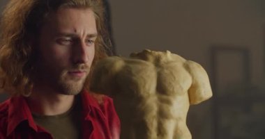 Genç, uzun saçlı heykeltıraşın çömlek kilinden insan gövdesine dönüşmesini yakından izleyin. Konsantre olmuş milenyum insanı, sanat objesi yaparken yarattığı şeye bakıyor. Sanat eseri kavramı.