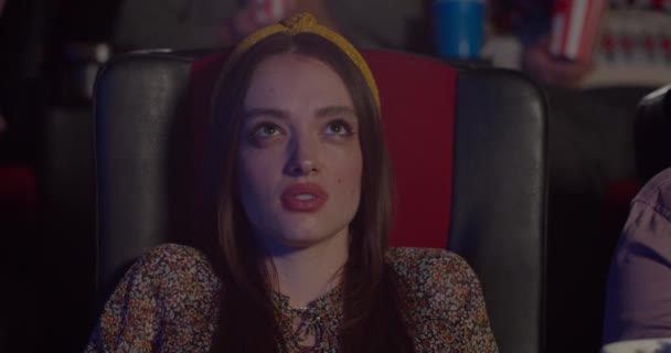 Close up of terrified pretty girl watching horror film at cinema. Millennial woman reacting to scary moment in movie by covering face with hand while sitting in chair. Concept of entertainment. — Stock Video