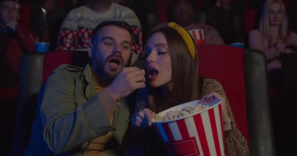 Blisko dziewczyny kradnącej popcorn swojemu chłopakowi podczas oglądania filmu w kinie.Para dobrze się bawiąca i śmiejąca podczas randki w kinie — Wideo stockowe