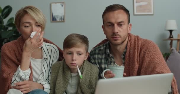 온라인상의 상담중에 엄마, 아빠, 아들이 독감에 대해 이야기하는 모습을 가까이서 볼 수있습니다. 가족들은 집에서 소파에 앉아 노트북 화면을 보고 있습니다. 원격 의료의 개념. — 비디오