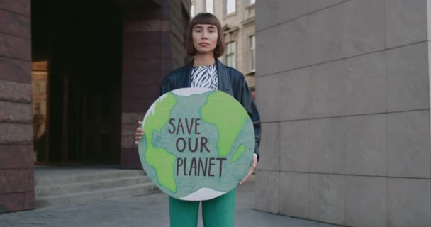 Mladá žena drží model Země s psaním zachránit naši planetu.Millennial dívka bojující proti znečištění životního prostředí, zatímco stojí na ulici.Concept ochrany životního prostředí Přiblížit. — Stock video