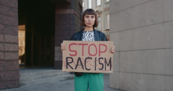 Millenijna dziewczyna wspierajaca kampanie antyrasistowska na ulicy miejskiej.Mloda aktywistka trzymajaca w rekach sztandar bez wyrazenia rasizmu. Pojęcie równości praw człowieka i tolerancji. — Wideo stockowe