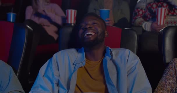 在电影院看喜剧片的快乐笑脸人的近照。一个英俊的非洲小伙子坐在电影院里笑着。娱乐的概念。积极的情绪. — 图库视频影像