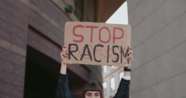 Jovem levantando cartaz sem frase racismo. Millennial hipster menina golpeando contra o racismo e intolerância, enquanto de pé na rua. Conceito de igualdade de direitos humanos. — Vídeo de Stock