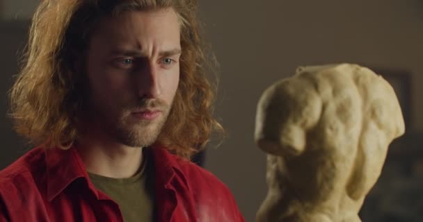 Vue rapprochée du jeune homme sculpteur tournant et touchant le torse humain de gypse. Homme concentré millénaire regardant sa création tout en faisant de la sculpture d'art dans l'atelier d'art. Concept d'oeuvre d'art. — Video