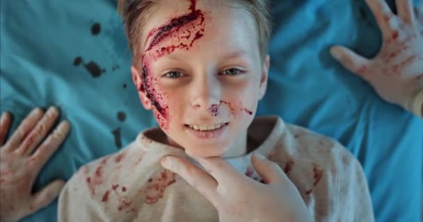 Маленький хлопчик з кров'ю і травмами голови посміхається, лежачи на лікарняному носику. Парамедичний контрольний пульс хлопчикові з травмами на шляху до операційної кімнати. Концепція охорони здоров'я . — стокове відео