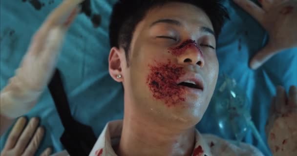 Blick von oben auf einen blutüberströmten Asiaten, der im Krankenwagen zur Besinnung kommt. Junger Mann mit Kopfverletzungen liegt auf Krankenhaustrage, während Sanitäter Sauerstoffmaske im Gesicht aufsetzen. — Stockvideo