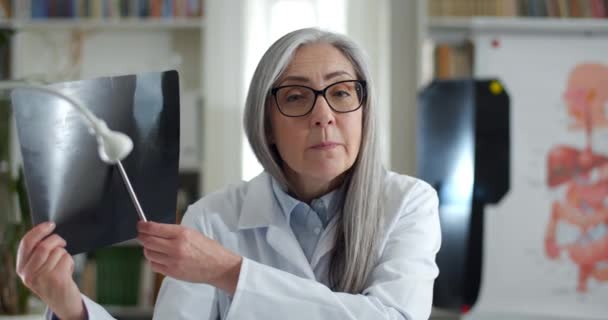 Crop view of professional woman in glasses and white rob showing x ray picture and talking while having video online call. Female doctor looking to camera. Concept of telehealth. — Stock Video