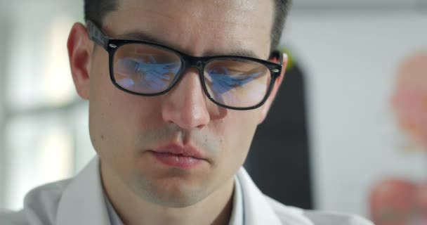 Gros plan d'un médecin masculin fatigué enlevant des lunettes et massant les yeux. Homme en robe professionnelle blanche regardant surmené alors qu'il était assis à table dans un bureau médical. Concept personne travailleuse. — Video