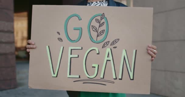 Mãos femininas segurando Go sinal vegan enquanto está em pé na rua vazia. Visão de perto da pessoa que promove o vegetarianismo e estilo de vida saudável. Conceito de Go Green e eco. — Vídeo de Stock