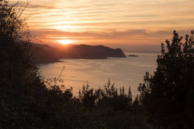 San Juan de Gaztelugatxe yakınlarındaki turuncu gökyüzü ile gün batımı Bermeo, Vizcaya, Bask Ülkesi, İspanya, Avrupa 'da bir adada yer almaktadır.