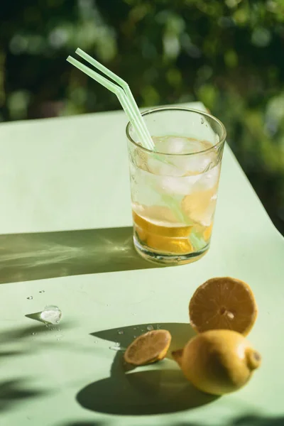 glass with refreshing drink with ice, lemon and straws, on a green background. Summer drink.