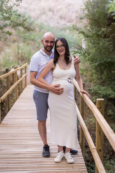 Cheerful Caucasian couple on maternity shoot in a wooden bridge