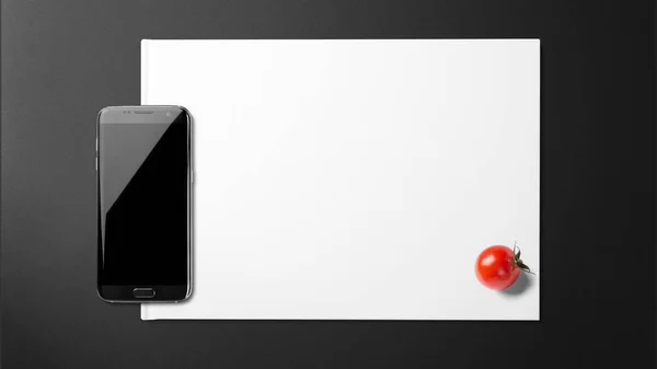スマート フォンで黒い背景に紙の上のトマト — ストック写真
