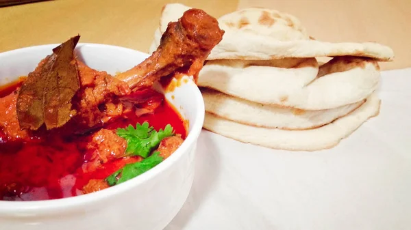Chicken curry masala spicy curry meat food in a white bowl with naan bread on wooden background.