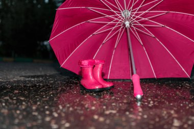 Islak şemsiye ve ıslak asfalt üzerinde çocuk lastik çizmeler