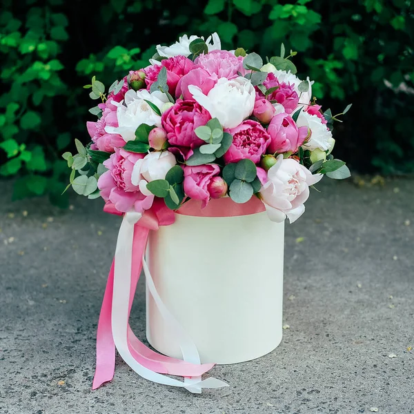 Gift flower box. Many white and pink peonies flowers and eucalyptus leaves in paper hatbox decorated with ribbons.