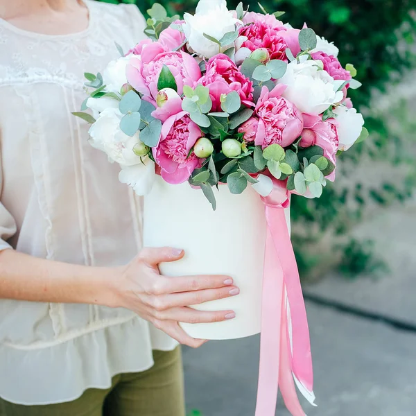 Gift flower box. Many white and pink peonies flowers and eucalyptus leaves in paper hatbox decorated with ribbons.