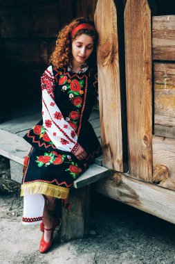 Genç Slavonic kadın geleneksel işlemeli kostüm ve verandada oturan kırmızı ayakkabılar