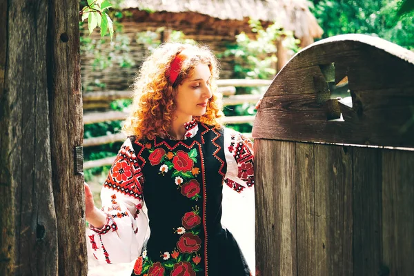Genç Slavonic kadında geleneksel kostüm işlemeli ve kırmızı ayakkabılar ile eski ahşap kapı açma çapraz