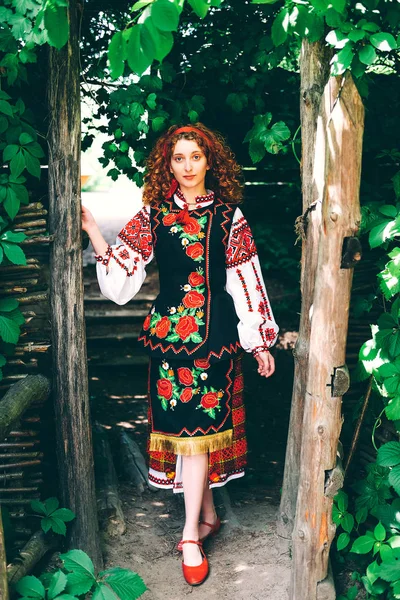 Genç Slavonic kadında geleneksel kostüm işlemeli ve kırmızı ayakkabılar ile eski ahşap kapı açma çapraz