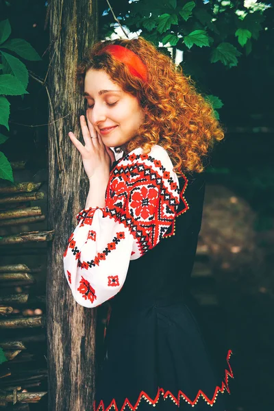 若いスラヴ語女性伝統的な刺繍の衣装と赤い靴の古い木製の門を開くクロス — ストック写真