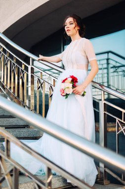 Sevimli Genç gelin gelin buketi ile peonies yapılan, gül, frezya çiçek ve giyen Beyaz tül düğün ayakta merdiven üzerinde giysi