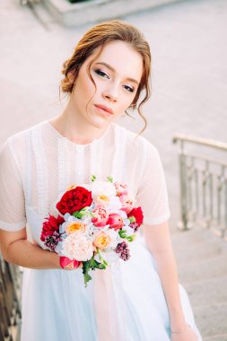 Sevimli Genç gelin gelin buketi ile peonies yapılan, gül, frezya çiçek ve giyen Beyaz tül düğün ayakta merdiven üzerinde giysi