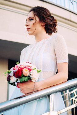 Sevimli Genç gelin gelin buketi ile peonies yapılan, gül, frezya çiçek ve giyen Beyaz tül düğün ayakta merdiven üzerinde giysi