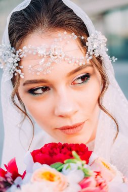 Beyaz duvak ve gelin buketi açık havada günbatımında poz tutan postiş güzel Doğu tarzı gelinle