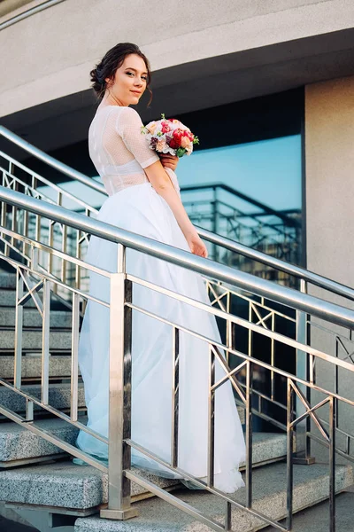 ブライダル ブーケと愛らしい若い花嫁は フリージアの花 身に着けている白のチュール ウェディング ドレス立って階段 — ストック写真