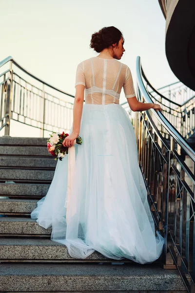 ブライダル ブーケと愛らしい若い花嫁は フリージアの花 身に着けている白のチュール ウェディング ドレス立って階段 — ストック写真