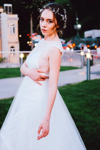 夏の夜の芝生の上に座っている白いドレスの魅力的な若い花嫁 — ストック写真
