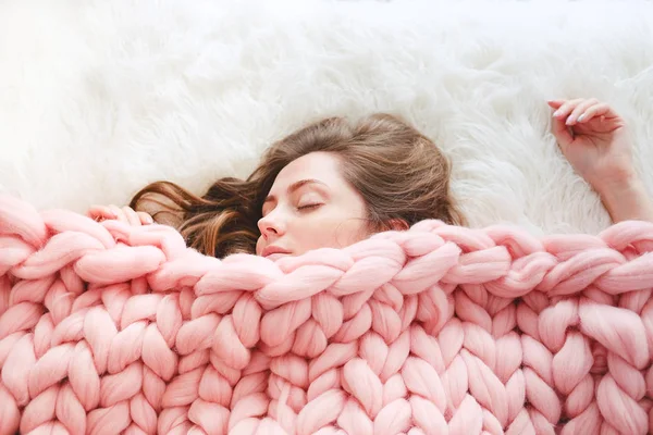 Young woman with long brown hair sleeping under warm knitted peach color throw blanket